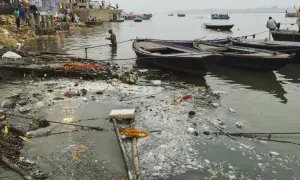 Rzeka Ganges, święta w hinduizmie, jest miejscem rytuałów i kremacji. Widać łodzie i ludzi na brzegu, ale też śmieci unoszące się na wodzie.