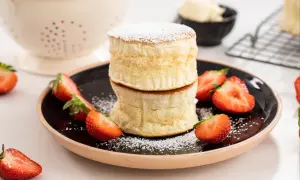 Två fluffiga amerikanska pannkakor staplade på en tallrik med färska jordgubbar och pudersocker.