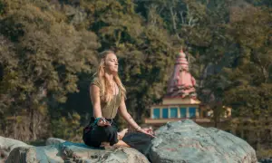 Mujer meditando en postura de loto sobre rocas, con un templo al fondo. Un momento de paz y el despertar de la conciencia.