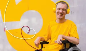 Giovane sorridente in carrozzina con cuffie gialle, un esempio di progetti di vita indipendente.