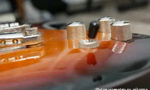 Metalowe potencjometry do gitary, błyszczące na pomarańczowo-czarnym korpusie.
