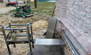 Baustelle mit Bagger, Maschine und Metallkonstruktion. Eine horizontale Sperrschicht aus Metallblech schützt die Ziegelwand.