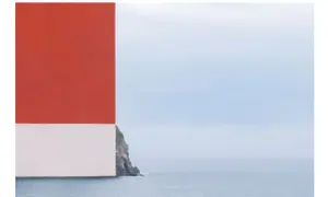 Scogliera rocciosa con mare calmo e cielo azzurro, con un blocco rosso e bianco che incombe a sinistra. Opera di Alberto Selvestrel.