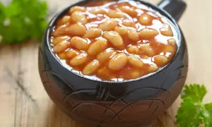 Un bol de haricot blanc en sauce tomate, garni de persil frais, sur fond de bois.