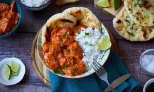 Ein Teller mit cremigem Butter Chicken, Reis und Naan-Brot. Garniert mit frischem Koriander und Limettenspalten.