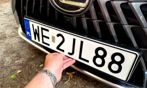 Dłoń poprawia tablicę rejestracyjną z numerem WE 2JL88.