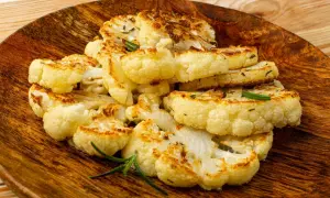 Tranches de chou-fleur entier au four, dorées et savoureuses, garnies de romarin frais sur une assiette en bois.