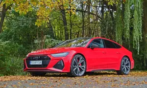Czerwone Audi RS7 Sportback zaparkowane na tle jesiennego lasu, z liśćmi na drodze.