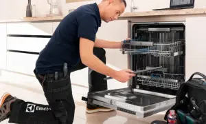 Serwisant w ubraniu z logo Electrolux naprawia zmywarkę. Electrolux to znana firma produkująca sprzęt AGD.