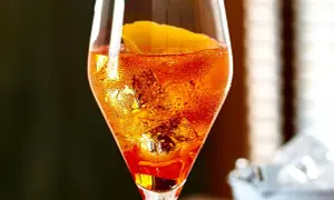 Ein Aperol Sour im Glas mit Eiswürfeln und Orangenzeste, Bläschen steigen auf.