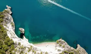 Vista aerea della cala della pipa, con scogliere bianche, vegetazione verde e mare turchese. Una barca lascia una scia sull'acqua.