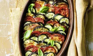 Gebackenes Gemüse aus Auberginen, Zucchini und Tomaten in einer Auflaufform, garniert mit Basilikum.