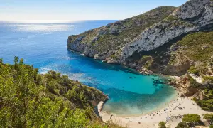 Bahía de aguas turquesas y arena dorada, rodeada de acantilados verdes. Un paraíso de playas bonitas con gente disfrutando del sol.