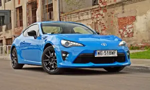 Niebieskie coupe Toyota GR86 z czarnymi felgami stoi przed zniszczoną ceglaną ścianą.