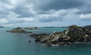 Îles rocheuses et mer turquoise près de Douarnenez, avec la Pointe du Raz en arrière-plan sous un ciel menaçant.