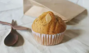 Un soffice muffin allo yogurt, guarnito con una mandorla, pronto per essere gustato con un cucchiaio di legno.