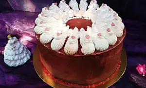 Elegancki tort w domu, ozdobiony bitą śmietaną i serduszkami. Obok stoi porcelanowa laleczka w sukni.