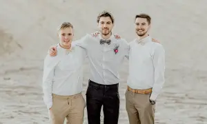 Trzech młodych mężczyzn w eleganckich koszulach i muszkach, gotowych do spełnienia obowiązków świadka na weselu.
