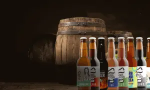 Bottiglie di birra artigianale davanti a botti di legno, un'atmosfera da keller pub.