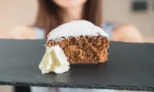 Una fetta di pan di spagna al cacao, soffice e spolverata di zucchero a velo, servita con panna montata su una lavagna scura.