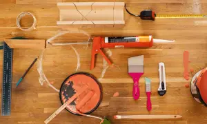 Pistolet à mastic, rouleau, pinceaux et pot de peinture orange sur un établi en bois.