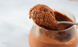 Un cucchiaio raccoglie una porzione generosa di soffice mousse al cioccolato da un bicchiere trasparente.