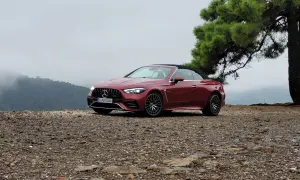 Czerwony kabriolet Mercedes-AMG CLE 53 na kamienistym podłożu, z drzewem i mglistymi górami w tle.