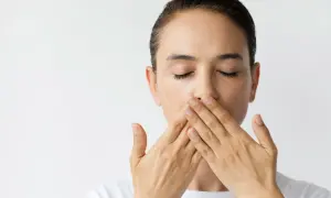 Donna con occhi chiusi copre la bocca con le mani, un'espressione che suggerisce una bocca amara o un segreto.