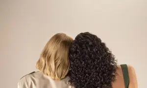 Due donne, una con capelli biondi lisci e l'altra con capelli scuri ricci, si abbracciano. La domanda è quanto dura una tinta permanente.