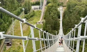 Menschen spazieren über den Willingen Skywalk, eine Hängebrücke mit Blick auf eine Skisprungschanze und bewaldete Hänge.