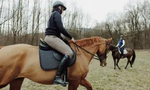 Dwie osoby na koniach w terenie, jedna bliżej, druga dalej.