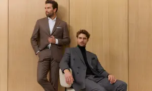 Zwei Männer in eleganten Anzügen vor Holzvertäfelung. Der eine steht, der andere sitzt. Die perfekte sakko passform unterstreicht ihre maskuline Silhouette.