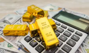 Sztabki złota na banknotach dolarowych i kalkulatorze symbolizują mądry gold investment.