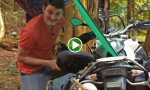 Mężczyzna przygotowuje motocykl do moto campingu w lesie, pakując bagaż.