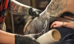 Manos enguantadas cubren un tatuaje recién hecho en el brazo con plástico. Aprende como cuidar un tatuaje recien hecho para una curación óptima.