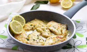 Scaloppine di pollo al limone in padella, guarnite con spicchi di limone fresco e prezzemolo tritato.