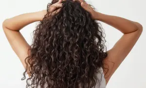 Vista trasera de una persona con un hermoso pelo rizado oscuro, sus manos acarician su melena.