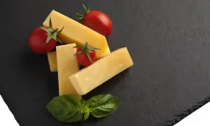 Kawałki żółtego sera, pomidorki koktajlowe i listki bazylii na czarnej desce. Czy to pecorino?