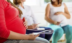 Tre gravida kvinnor sitter tillsammans, en i rött, en i vitt och en i ljusblått. De verkar vara på en kurs eller träff, kanske för att förbereda sig för gbs gravid.
