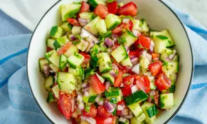 Frischer Tomaten-Gurken-Salat mit roten Zwiebeln und Kräutern, serviert in einer Schüssel.
