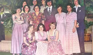 Grupa osób w eleganckich, pastelowych kreacjach. Widać długie suknie i garnitury, typowe dla lat 60 stylizacje.