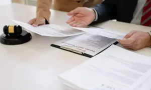 Dwie osoby analizują dokumenty, w tym weksel. Obok leży młotek sędziowski.