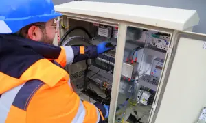 Elektryk z uprawnieniami SEP do 1kV pracuje przy rozdzielnicy elektrycznej, podłączając przewody.