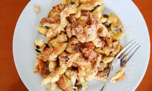 Ein Teller mit fluffigem Kaiserschmarrn mit Eischnee, bestreut mit Puderzucker und Zimt. Daneben eine Gabel.
