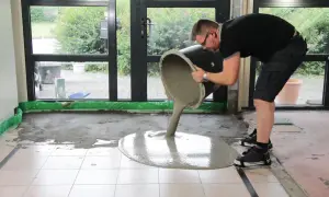 Mann gießt flüssigen Estrich aus einem Eimer, um den Boden auszugleichen.