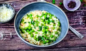 Ein cremiges Risi Bisi Rezept original, garniert mit frischer Petersilie und Erbsen. Daneben eine Schale geriebener Parmesan.