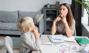 Terapeuta pokazuje dziecku, jak układać usta, gdy dzieci zaczynają mówić. Na stole litery i materiały do nauki.