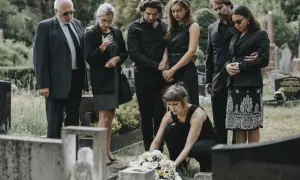 Trauernde Familie in schwarzer Beerdigungskleidung legt Blumen nieder.