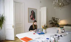 Młoda kobieta pracuje przy laptopie w jasnym pokoju. Czy Wielki Czwartek to święto? Zastanawia się, przeglądając notatki.