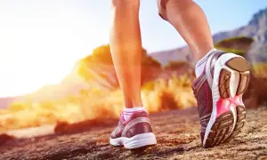 Nogi w butach sportowych stawiają kolejne kroki na kamienistej ścieżce. Słońce zachodzi za górami, tworząc ciepłą, złotą poświatę. Ile to 10000 kroków?